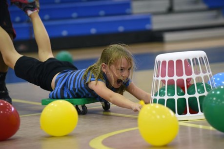 Student laying prone on scooter while pushing a basket of inflated balloons