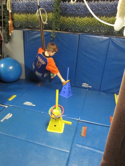 This boy is using a moon swing to pick up a ring from one stanchion and to place it on another stanchion that is placed further away
