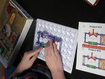 This photo shows a child building an electrical circuit by following a guide